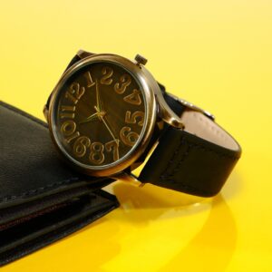 Elegant wrist watch with black leather strap displayed on yellow background closeup shot