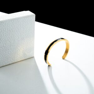 Gold bangle on white surface with black background, luxury jewelry